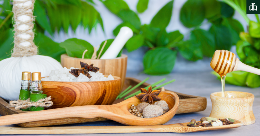 Cinnamon, dry ginger, black cardamom, javitri, long pepper and green leaves in mortar and pestle and scattered ayurvedic pills on white background