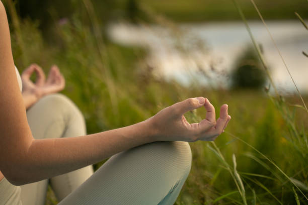 Close-up of the hands of a Caucasian woman meditating in the lotus position in nature by the pond.