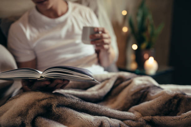 Close up of male on bed with open book and Tea. Man reading book on bed at home.